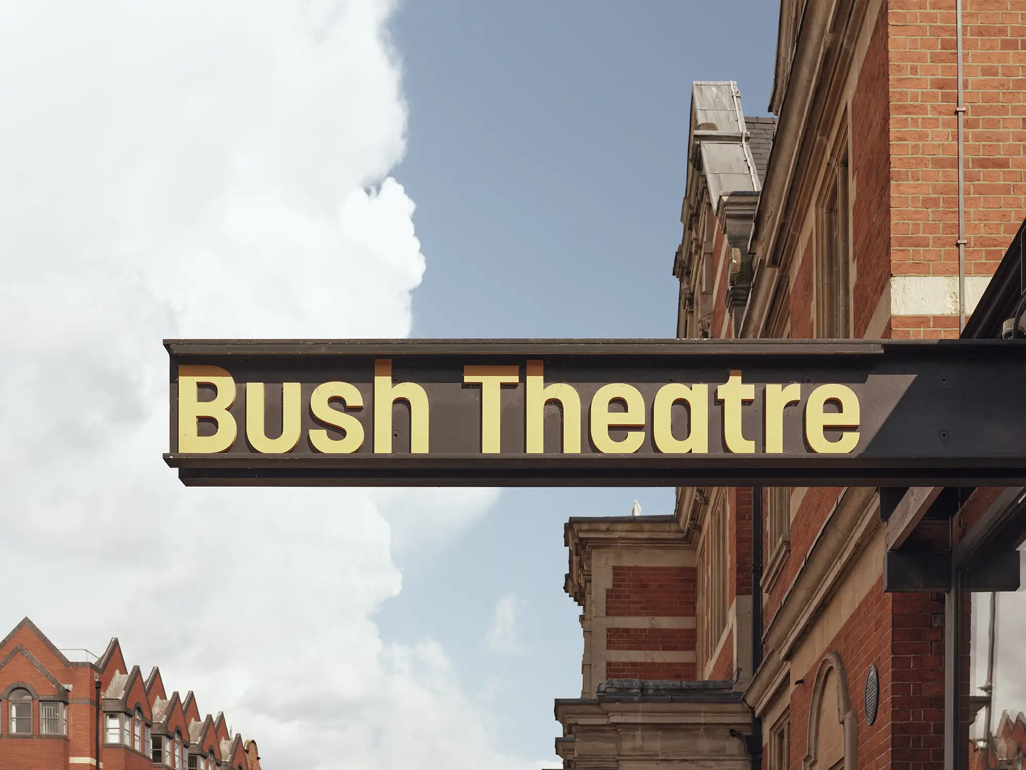 Close-up of the Bush Theatre external signage, a prominent black sign with illuminated yellow text.