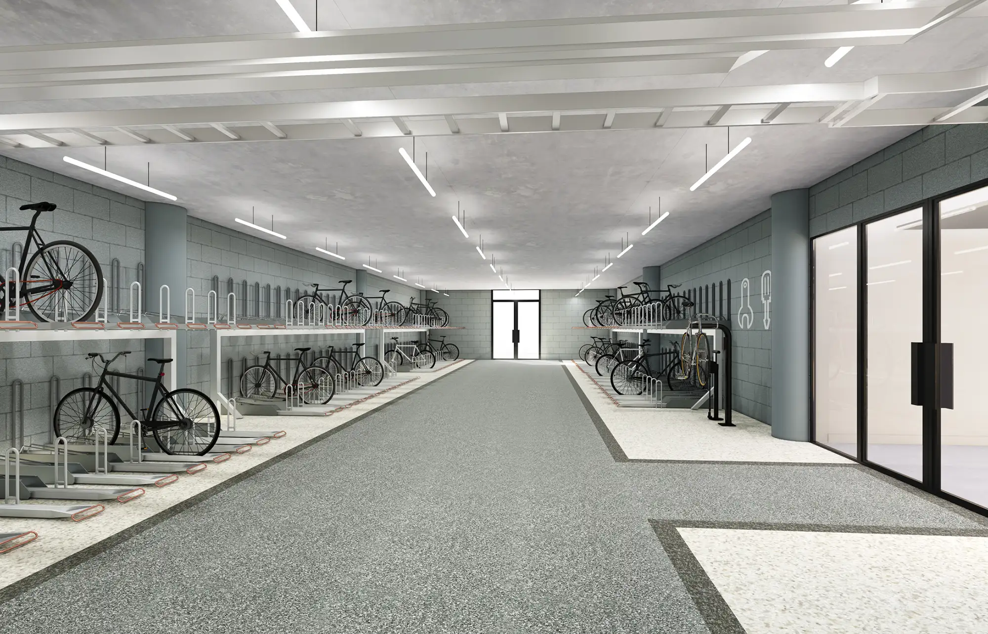 Modern bicycle storage room with rows of bikes parked in racks on either side of a gray speckled floor, under bright overhead lighting.