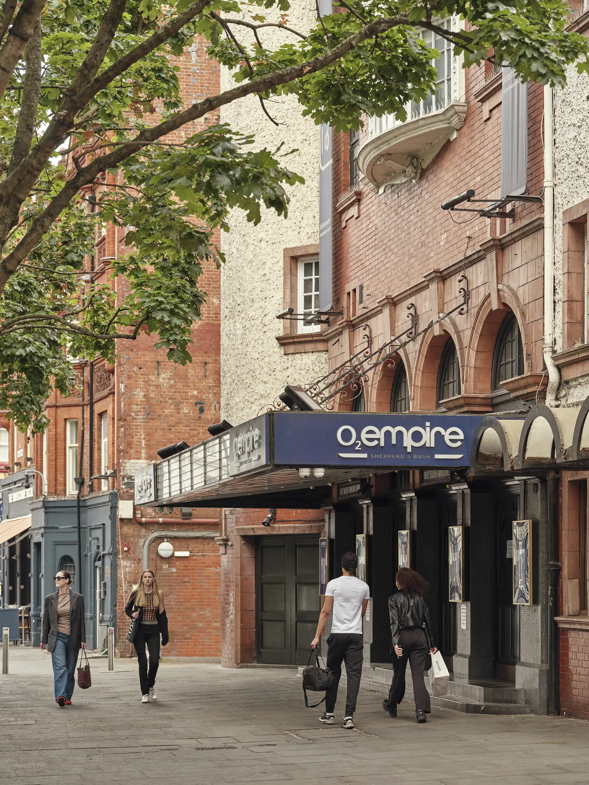 The exterior of O2 Shepherd's Bush Empire music venue with its blue sign and pedestrians walking past.