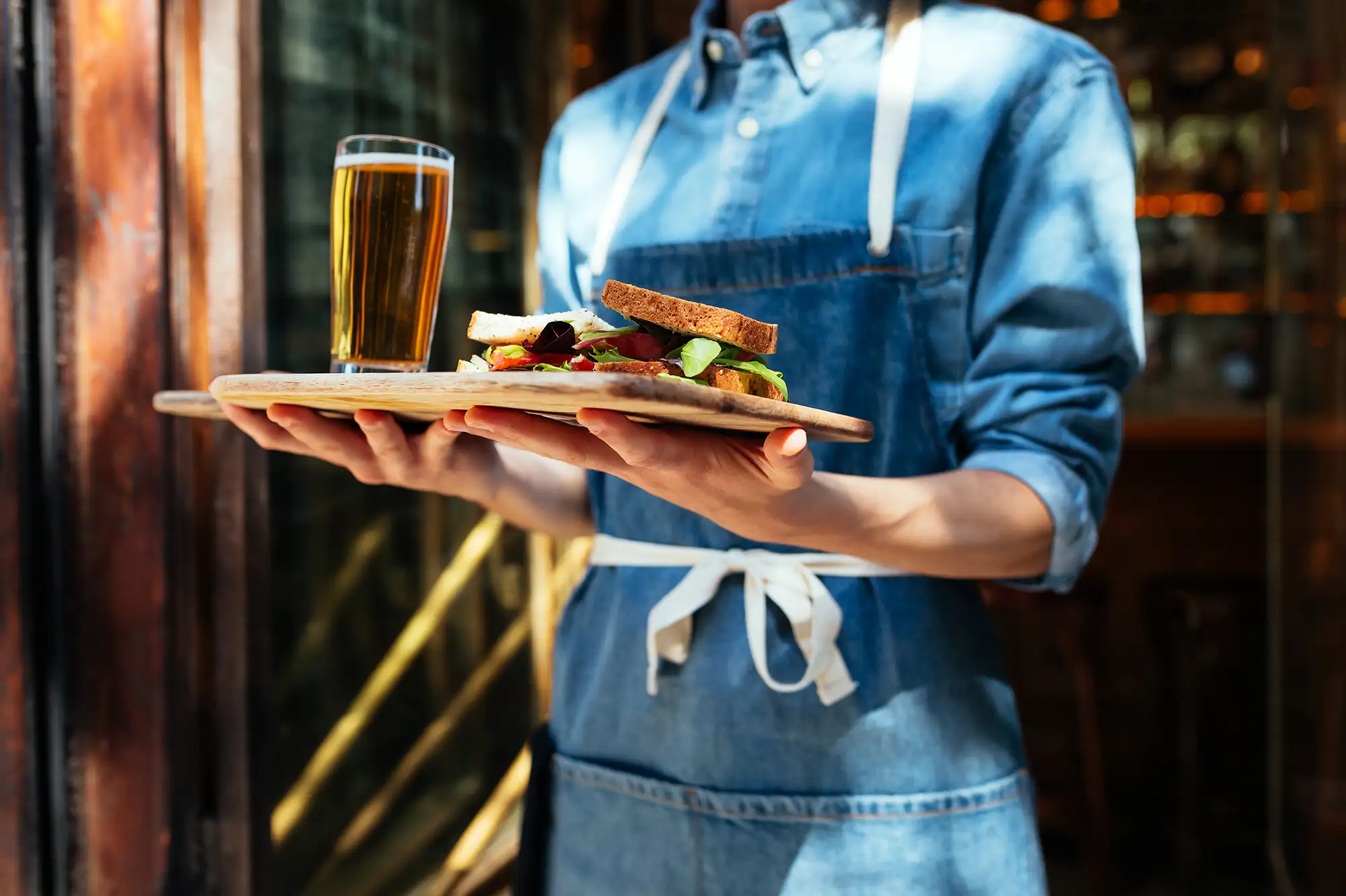Platter with sandwich and beer being carried by server in casual dining setting