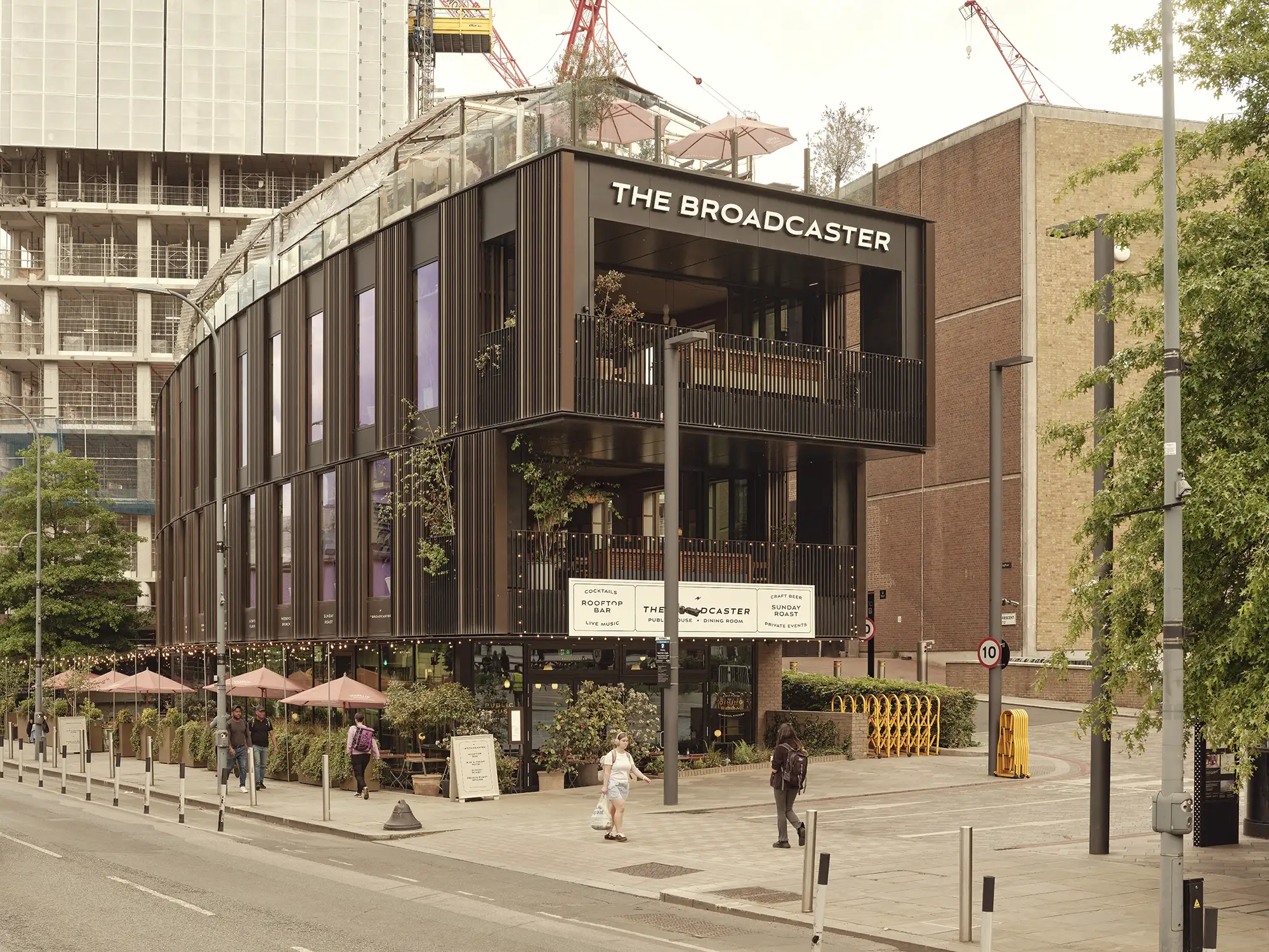 The Broadcaster building exterior with a modern black facade, outdoor seating, and construction in the background.