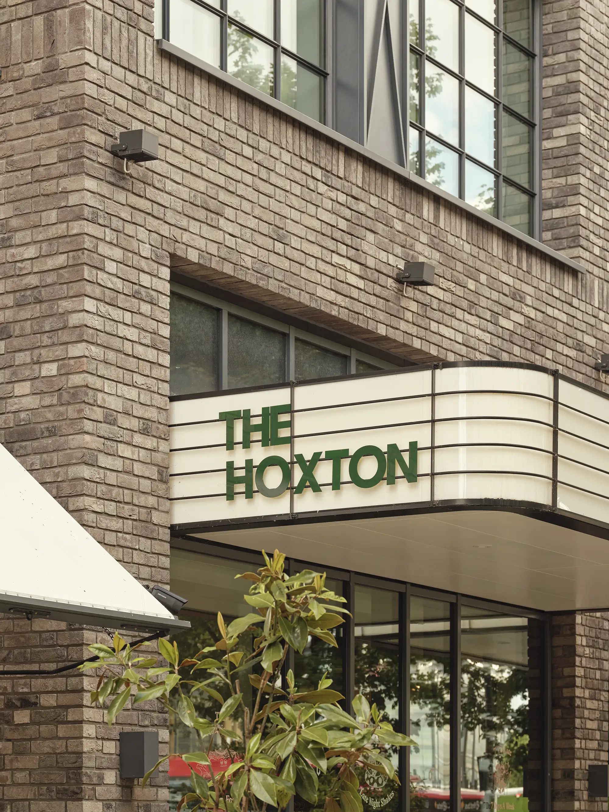 Close-up of The Hoxton hotel's external signage in green letters against a light-colored background.