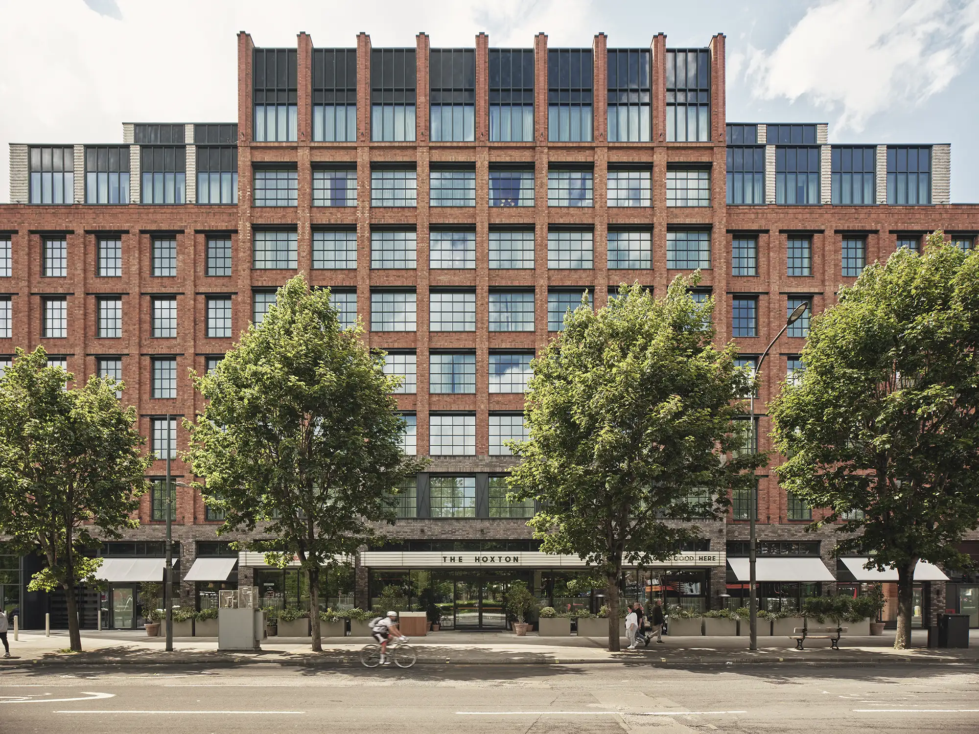 Front view of The Hoxton, Shepherd's Bush, a modern brick building with a grid of windows and street-level shops.