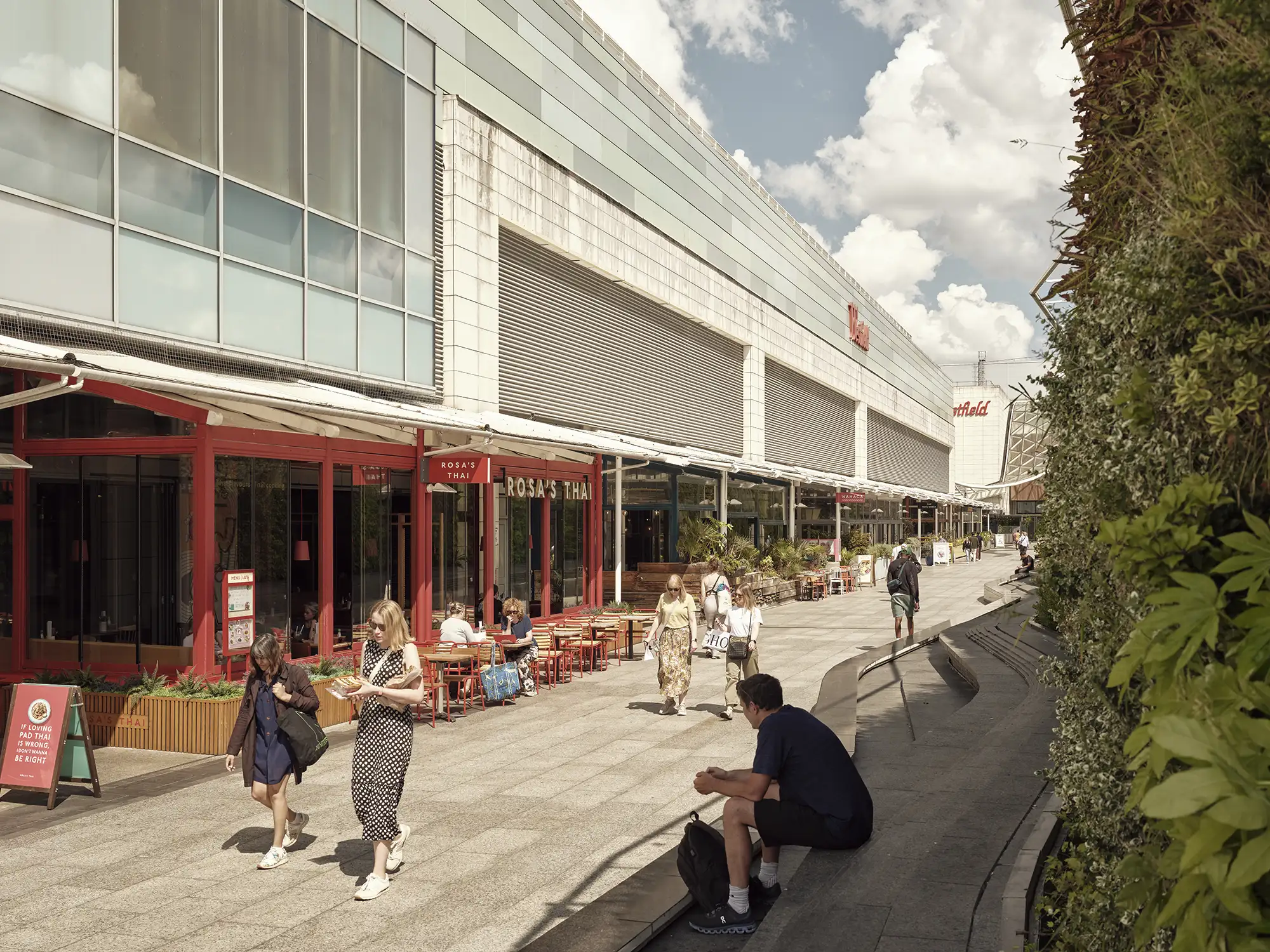 Outdoor dining area at Westfield London with people eating and walking alongside a living wall.