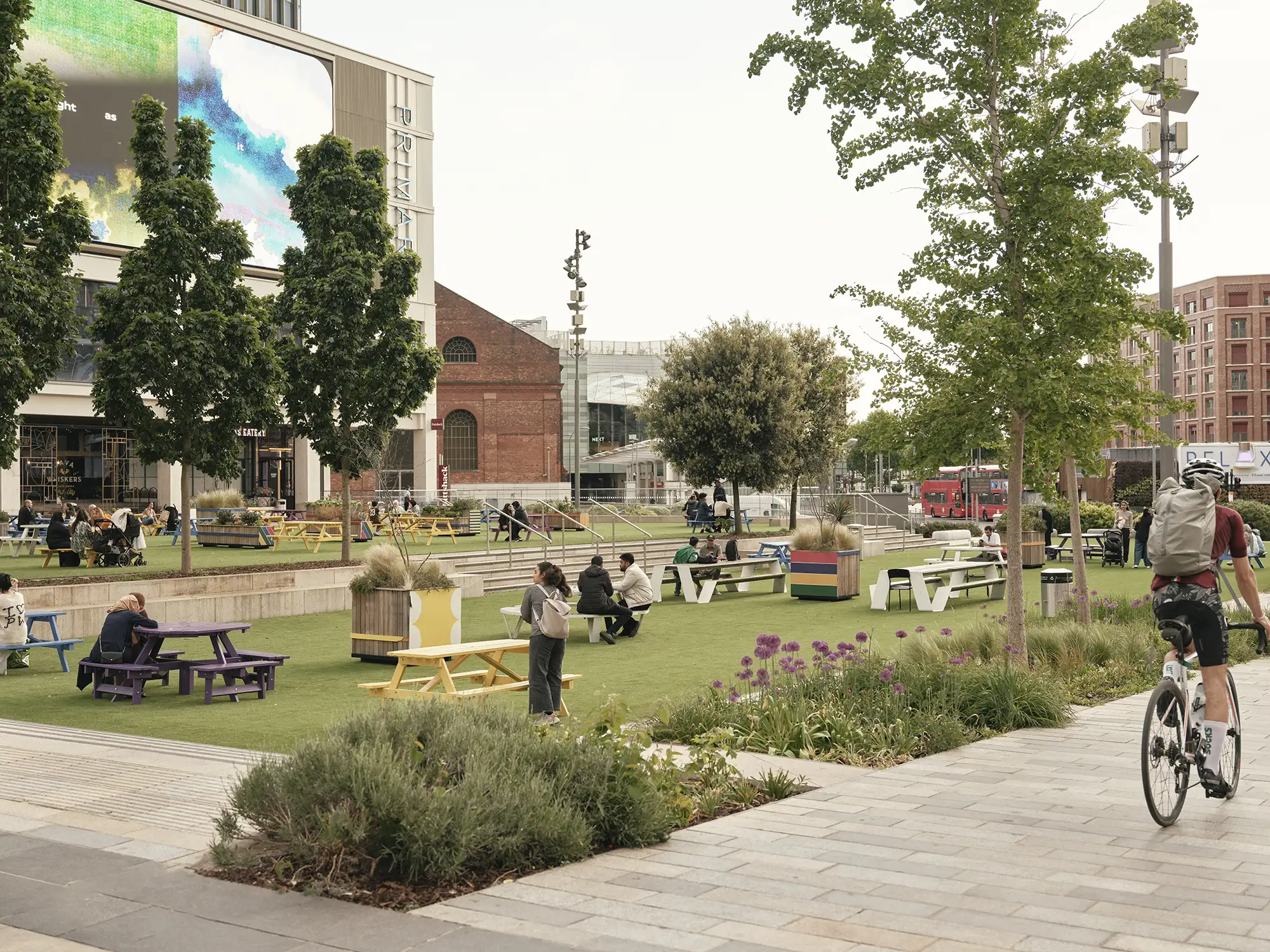 Westfield Square with faux grass, picnic benches of various colours, and people relaxing outdoors.