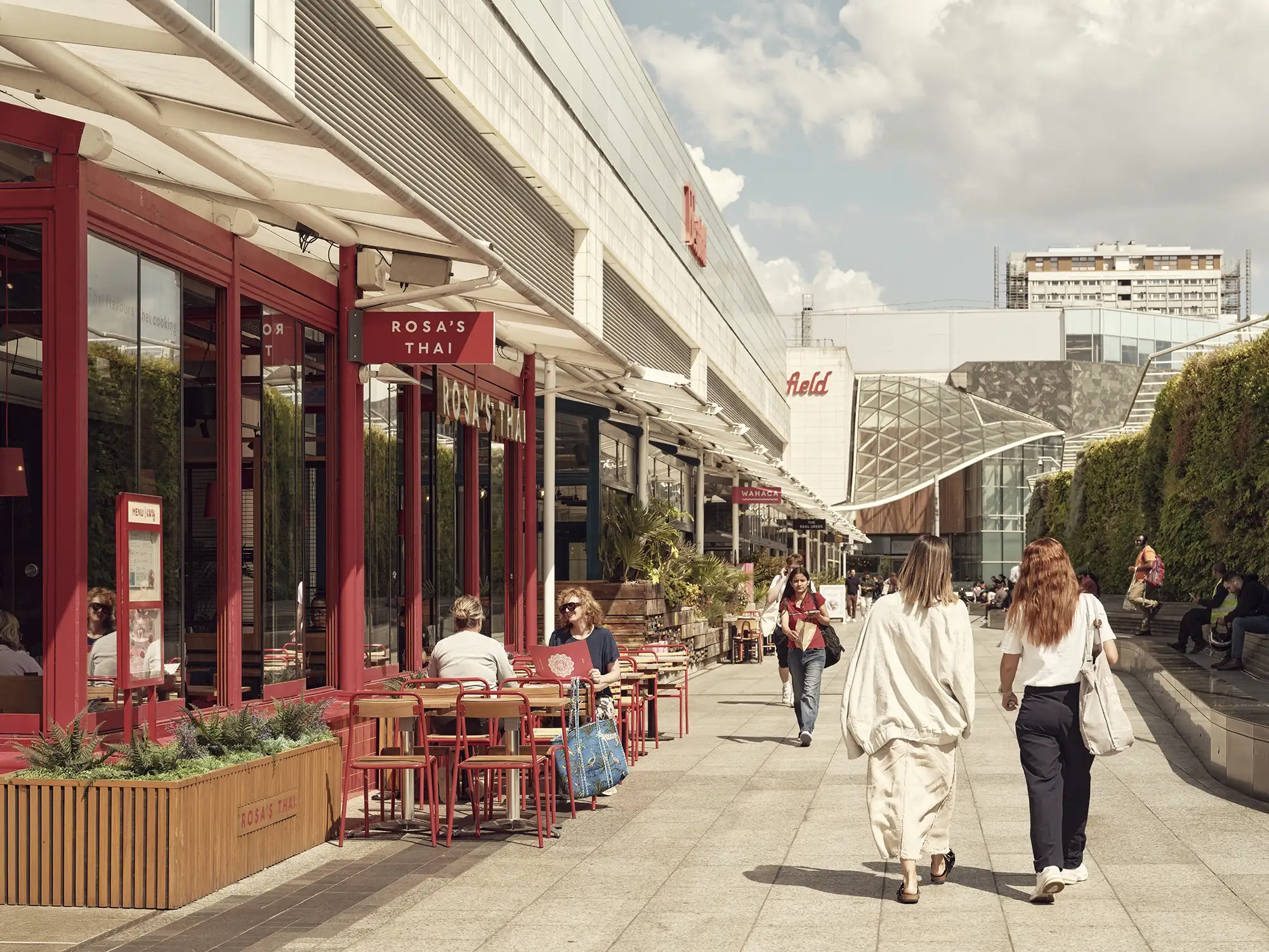 Outdoor dining area at Westfield Southern Terrace with red chairs and tables, and pedestrians strolling by.